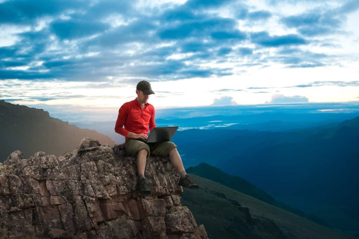 Man sitting on a top of a mountain with a laptop