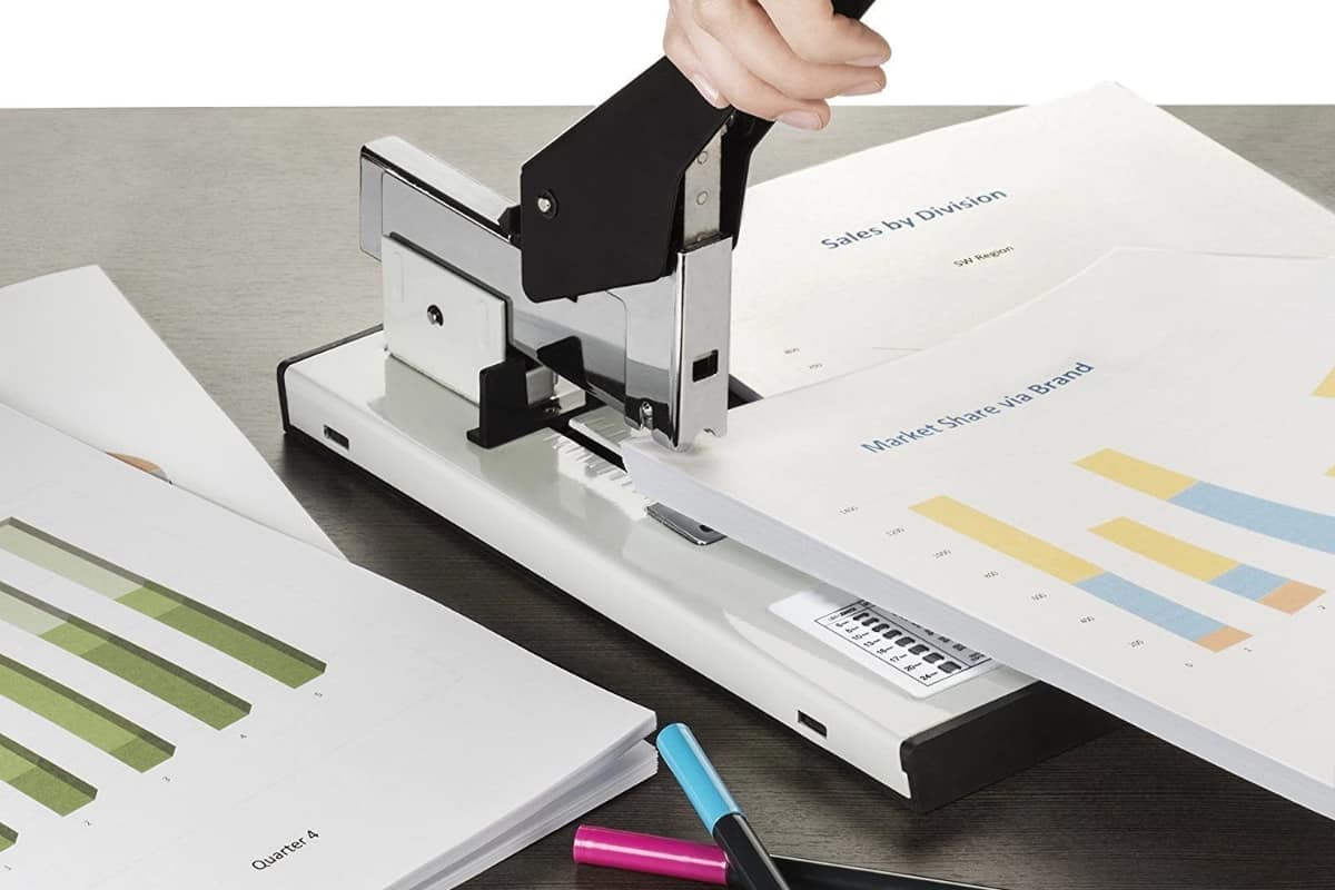 A woman stapling a big stack of paper with a heavy-duty stapler