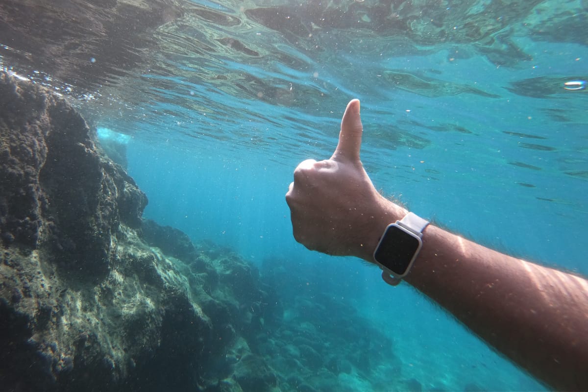 Close up of a hand with a waterproof smart watch underwater in the sea.