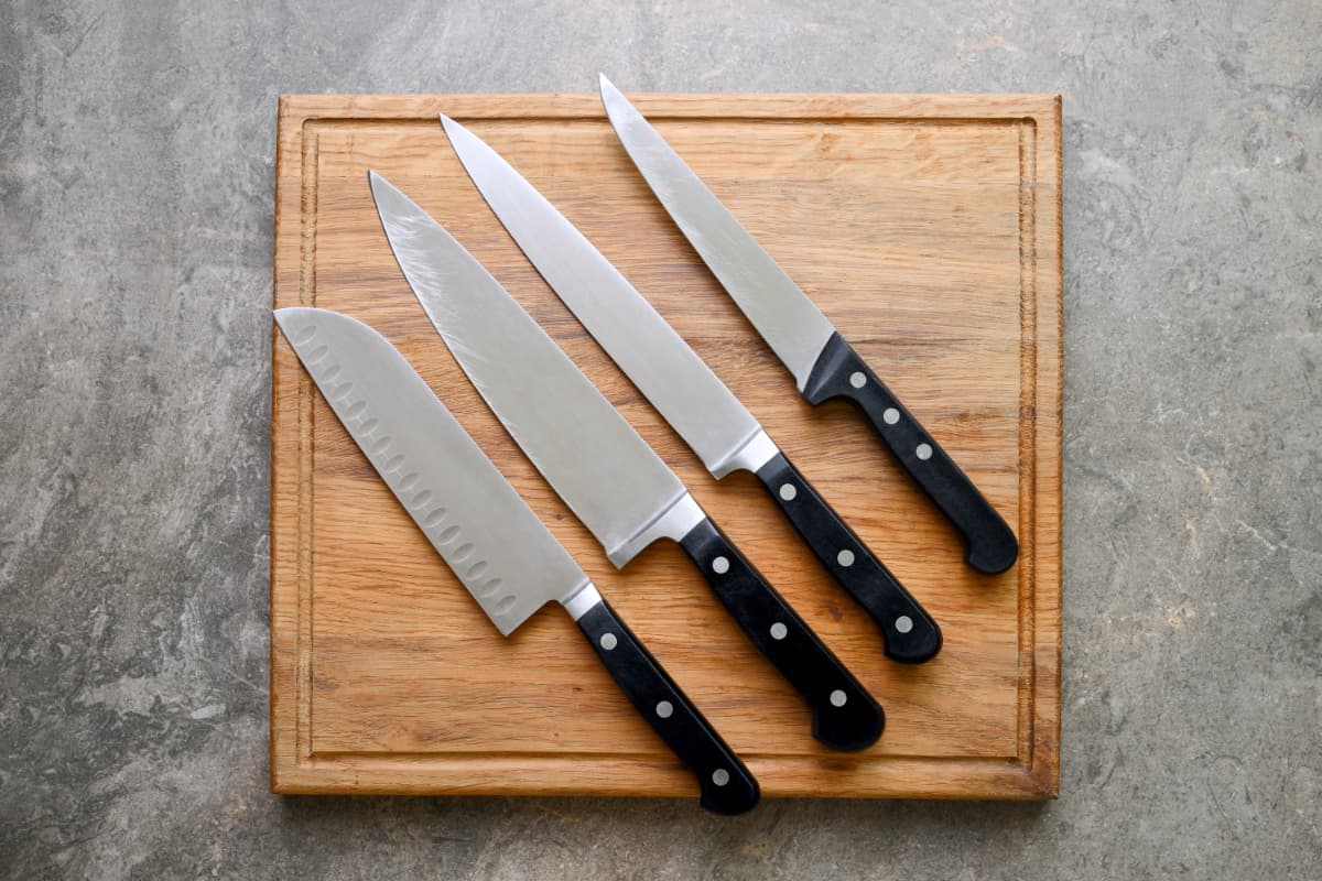 Kitchen knives set laying on wooden cutting board, flat lay, view from above