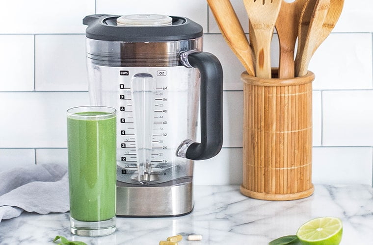 green smoothie next to a blender on a kitchen counter top