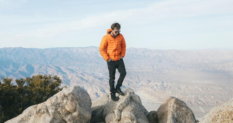 Man standing on a rock wearing an orange Eddie Bauer jacket