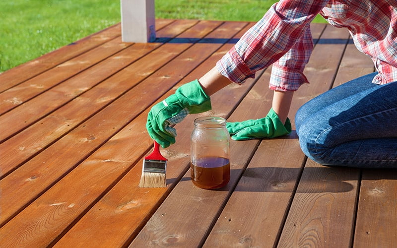 Woman applying protective varnish on a wooden deck