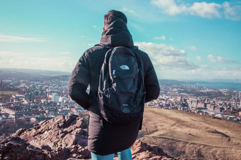 man standing on hill wearing north face backpack