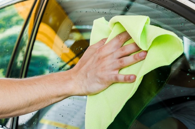 car washer holding green rag and cleaning car window-feature