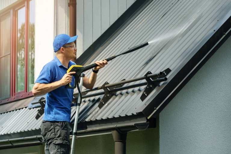 man cleaning a metal roof with a pressure washer - feature image