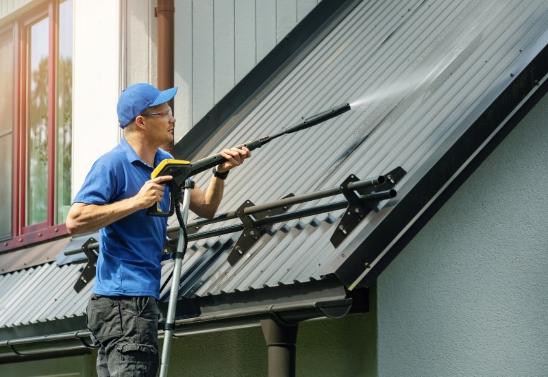 man cleaning a metal roof with a pressure washer