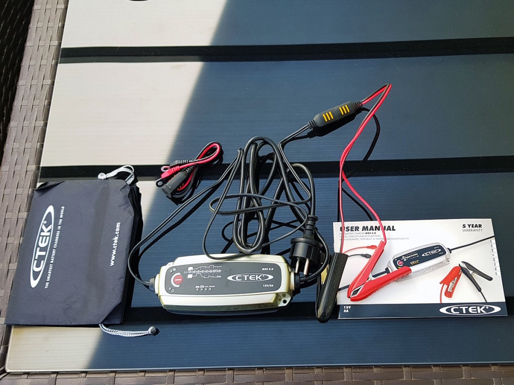 The CTEK MXS 5.0 charger, clamps, dust bag and owner's manual on a table