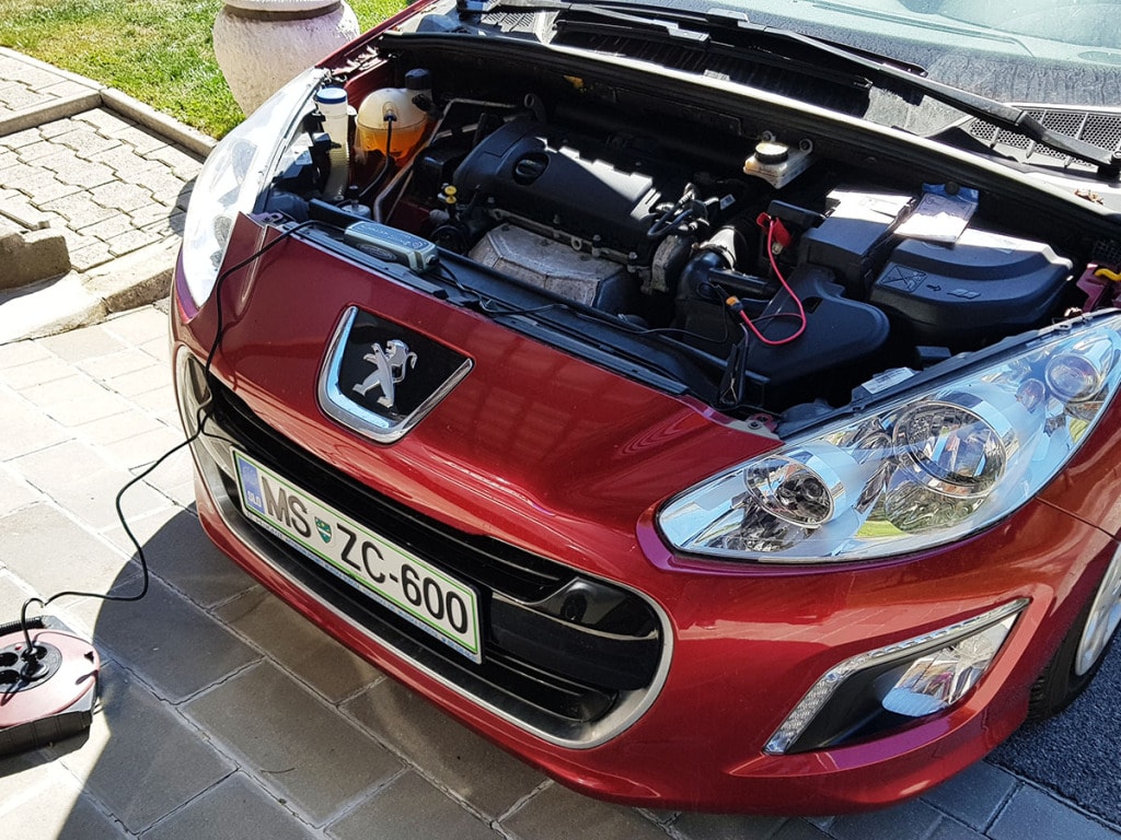 The front of Peugeot 308 with a CTEK MXS 5.0 charger attached to the battery