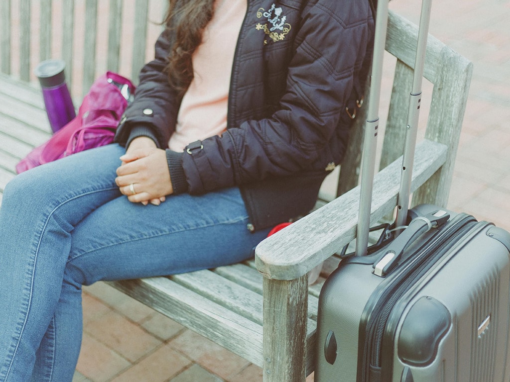 Woman on bench with hard side suitcase